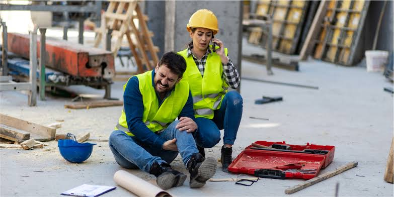 Injured construction worker receiving assistance from a colleague at a construction site.