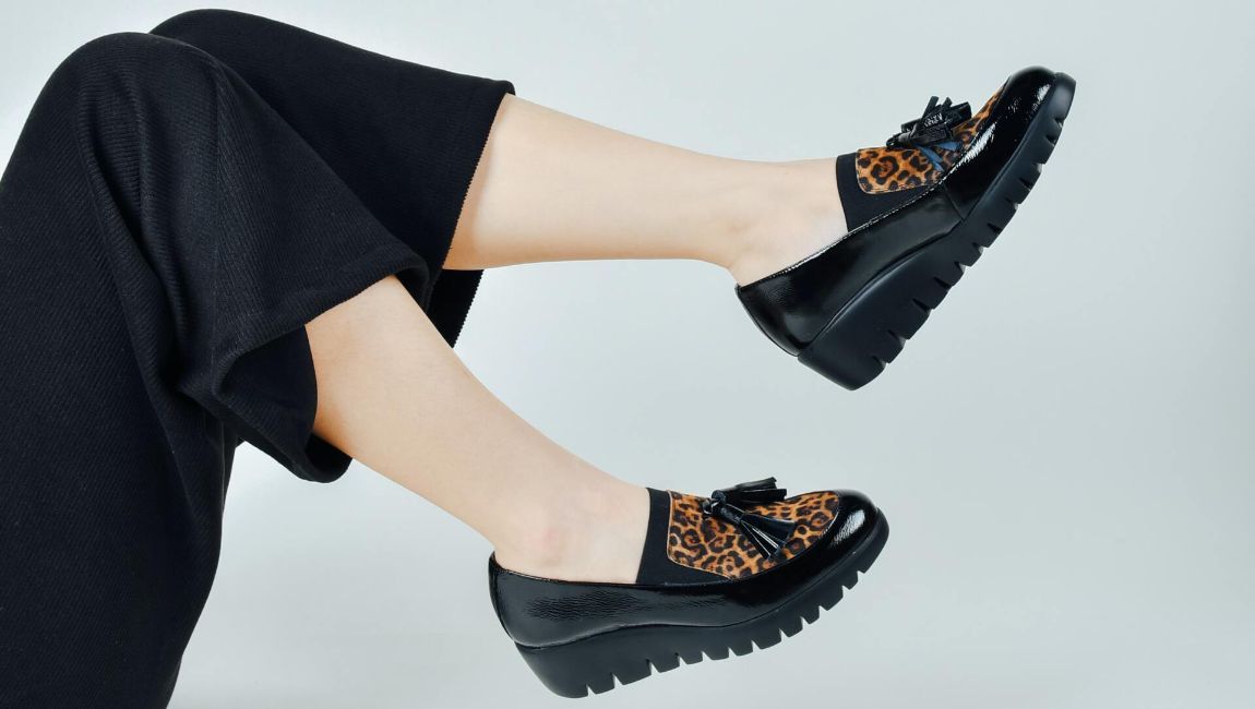 Black shoes with leopard print accents on feet, legs in black pants.
