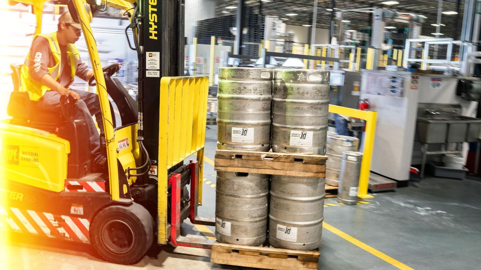 Forklift transporting a pallet of beer kegs inside a warehouse.