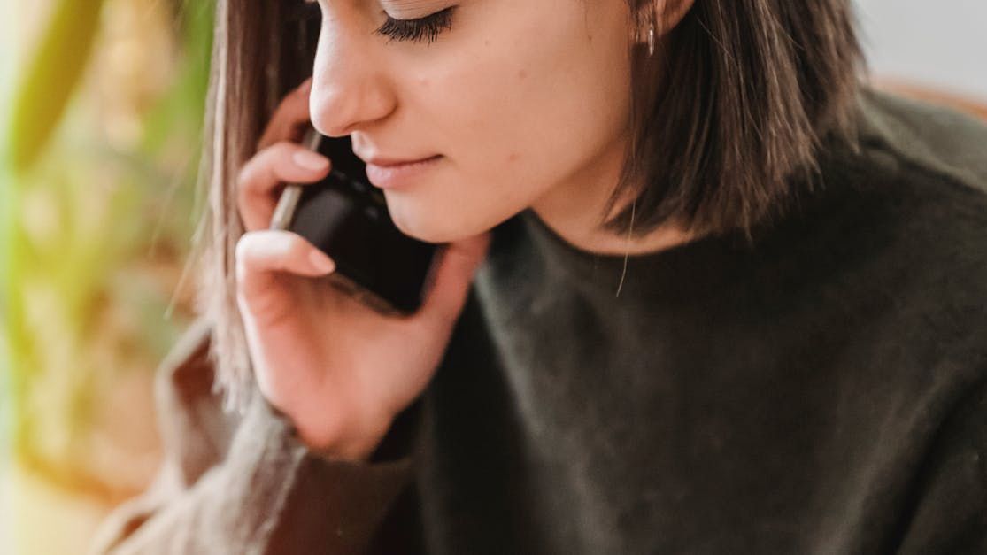 Woman with short brown hair, wearing a dark green sweater, talks on a cell phone.