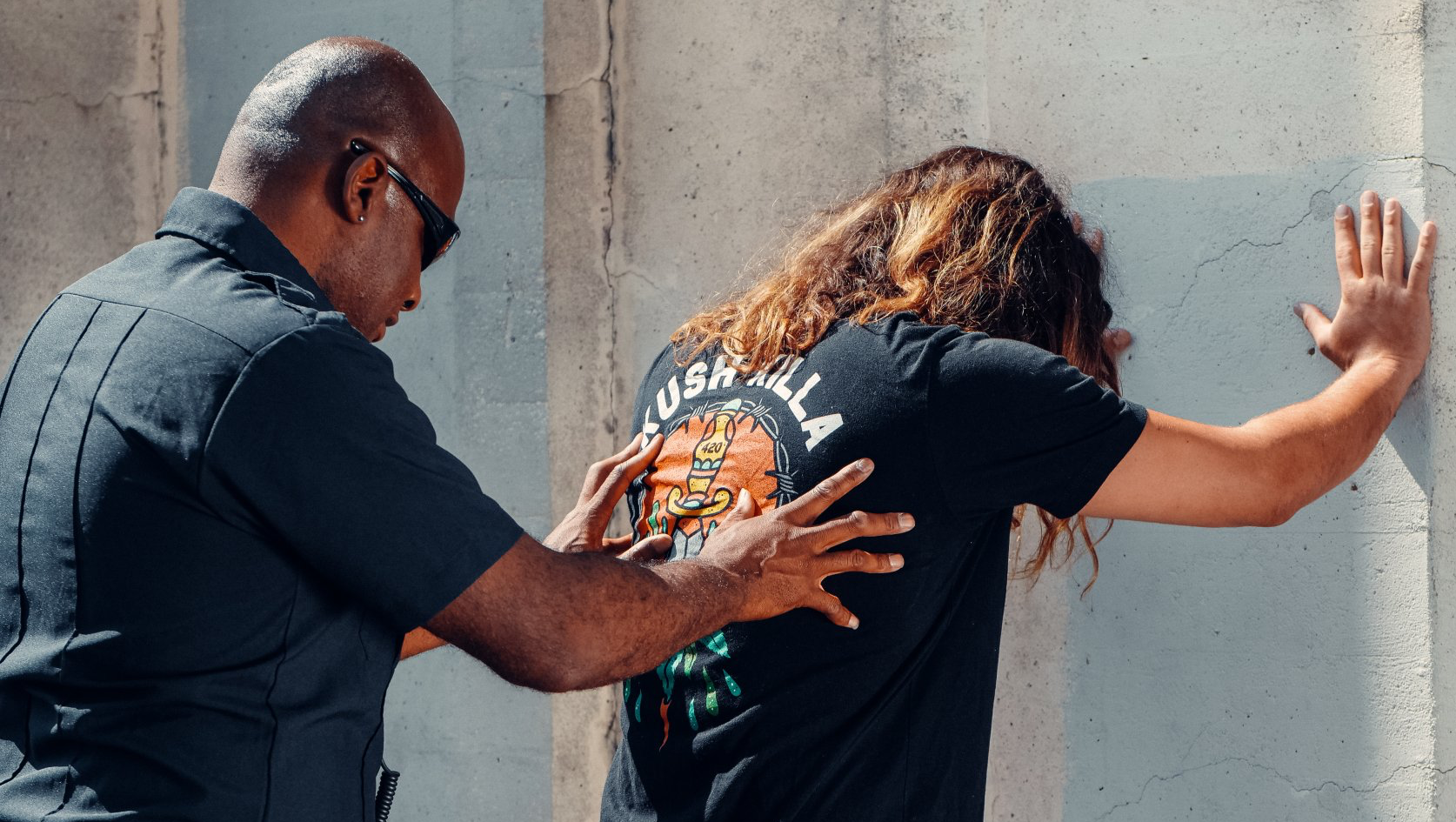Police officer patting down a person leaning against a wall.