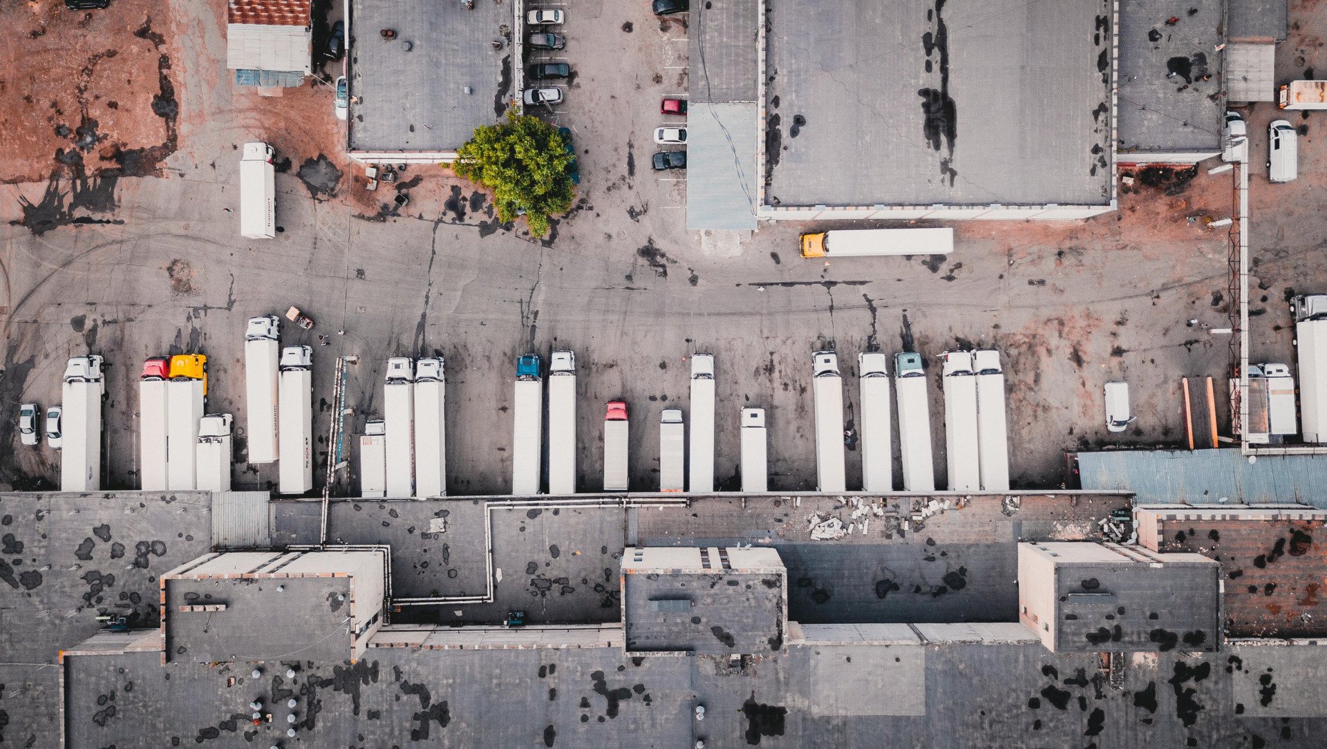 Overhead view of a loading dock with numerous parked semi-truck trailers, asphalt, and warehouse buildings.