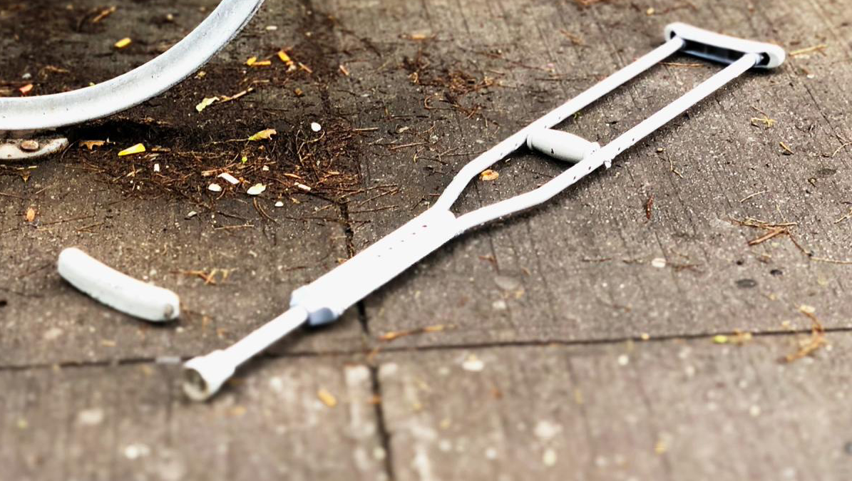 White crutch lying on the ground, with a detached rubber tip, next to a bicycle wheel.