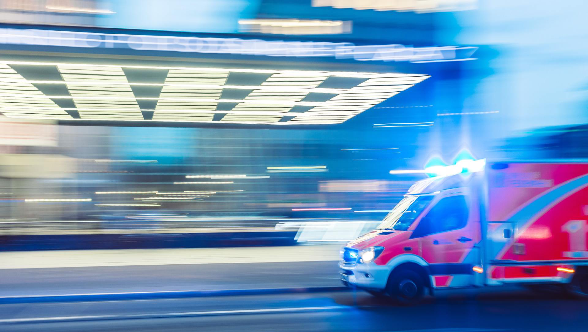 Ambulance with flashing blue lights speeding toward a building, blurred motion.