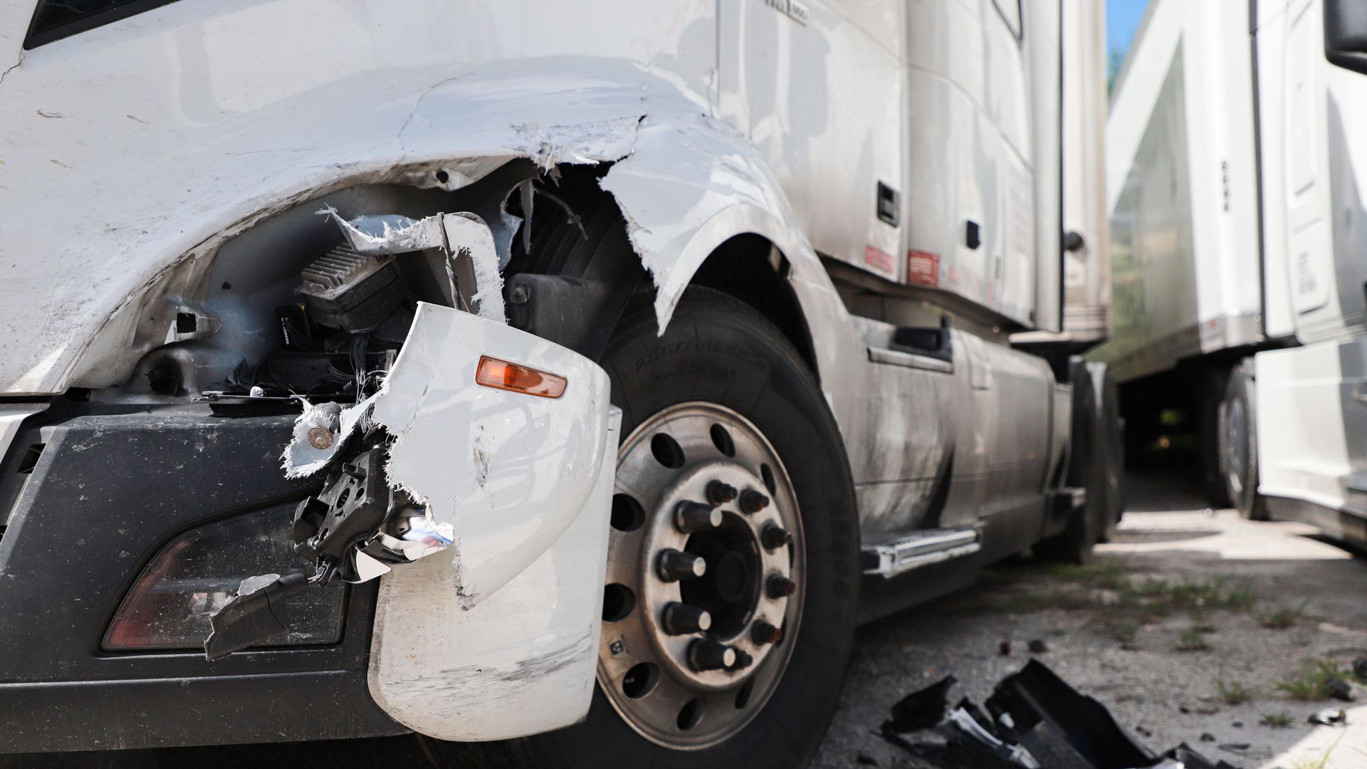 Damaged white semi-truck fender, close-up. Crushed area near the front tire.