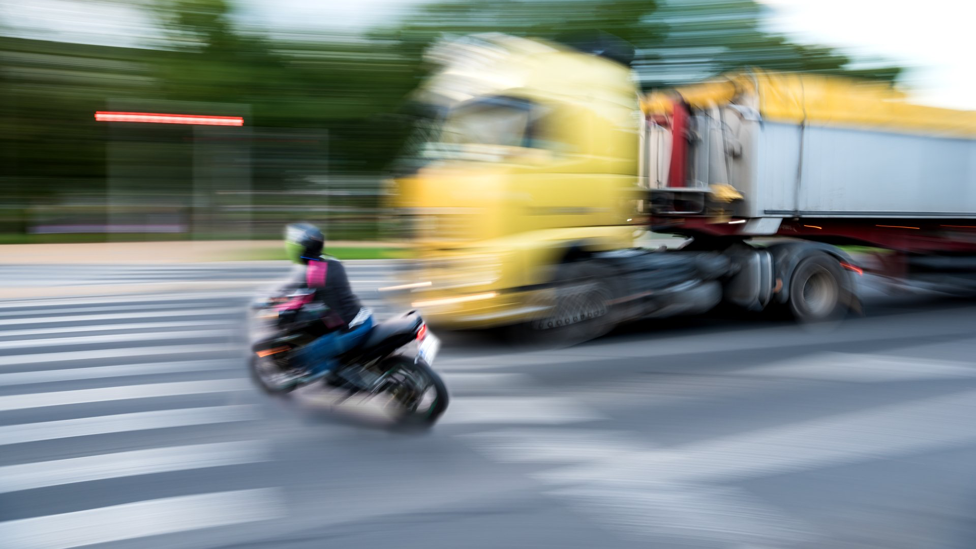 Motorcycle speeding across crosswalk, blurring with yellow truck.