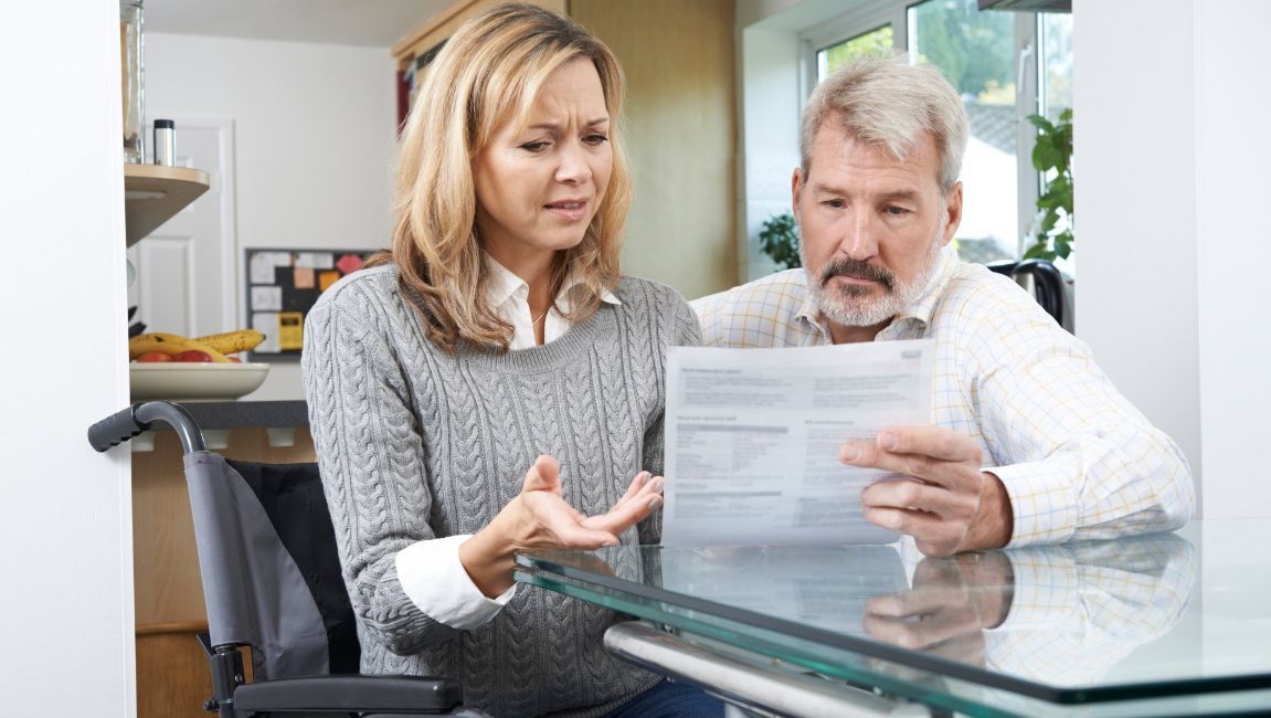 Woman in wheelchair and man review document, both looking concerned at table.