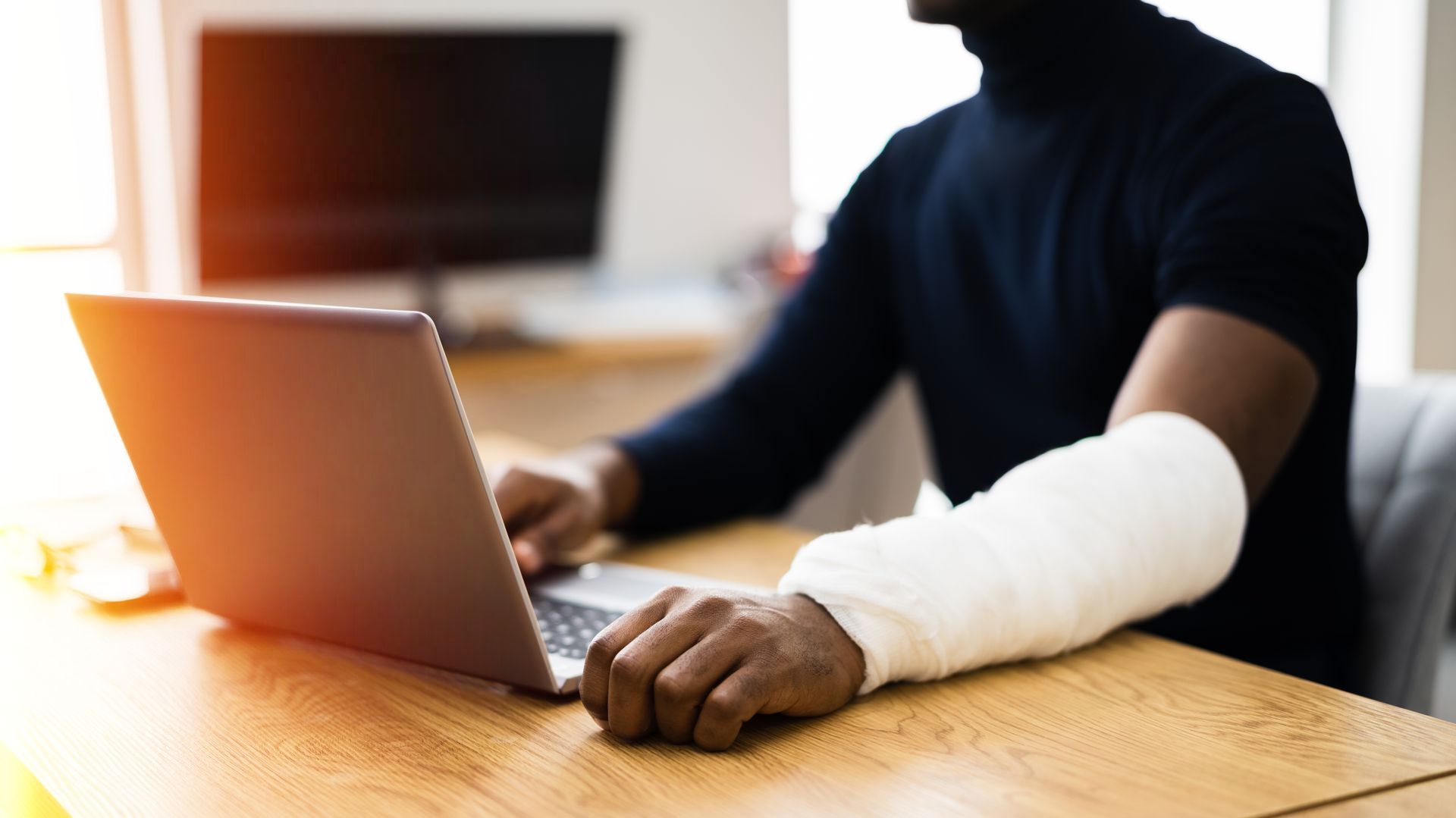 Man with cast on arm working at a laptop in an office setting.