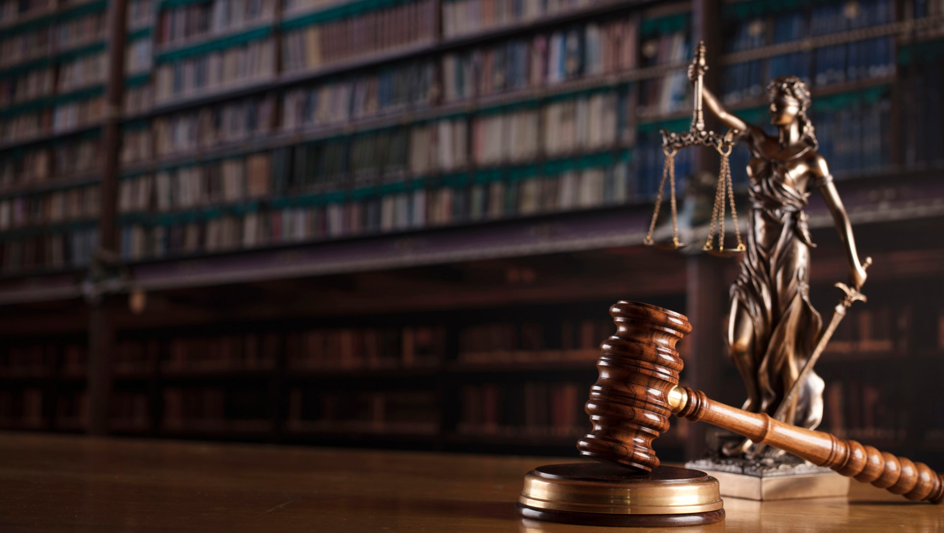 Statue of Lady Justice with scales and sword next to a gavel, against a blurred library background.