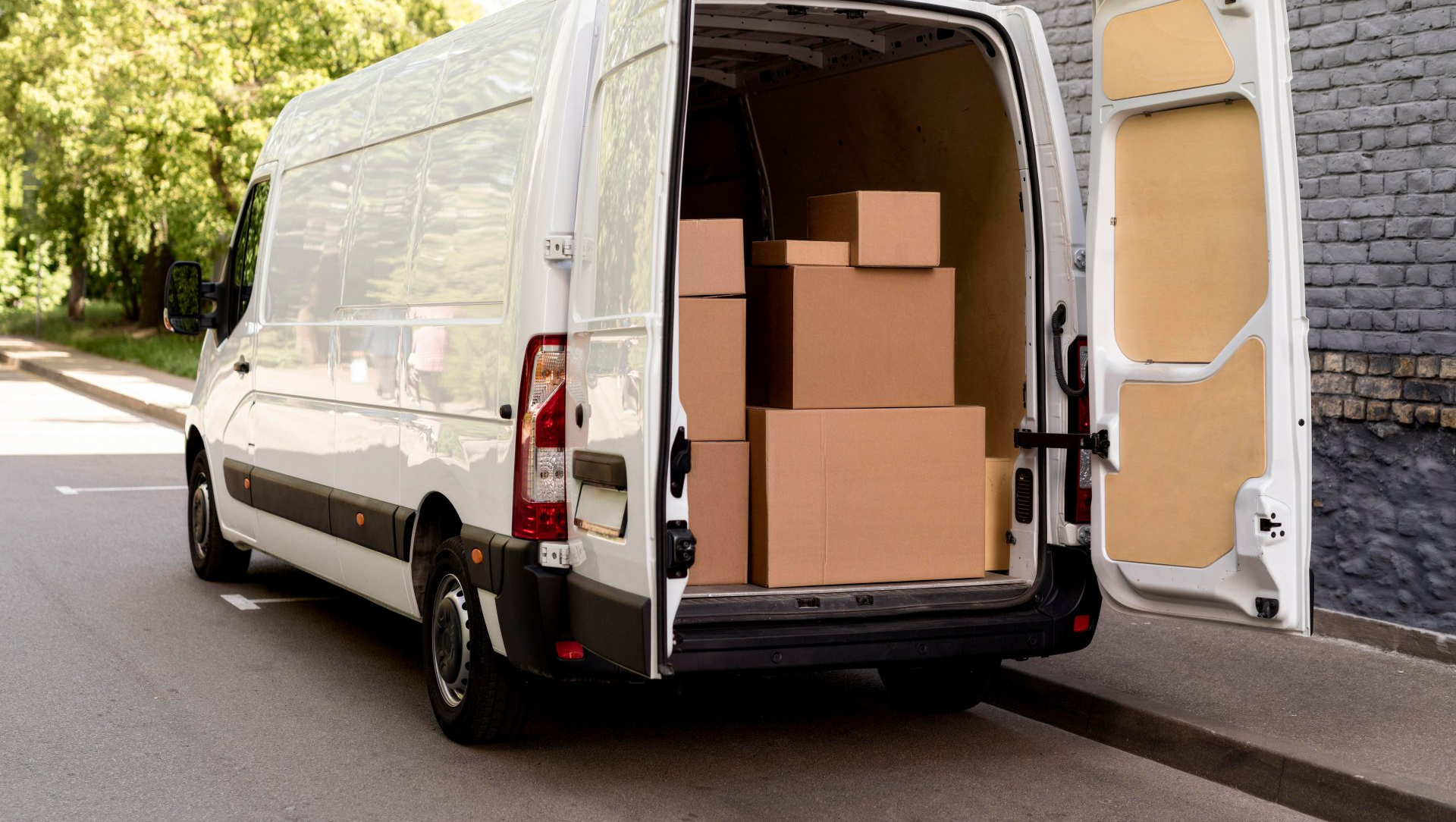 White delivery van with open back doors, packed with cardboard boxes on a city street.