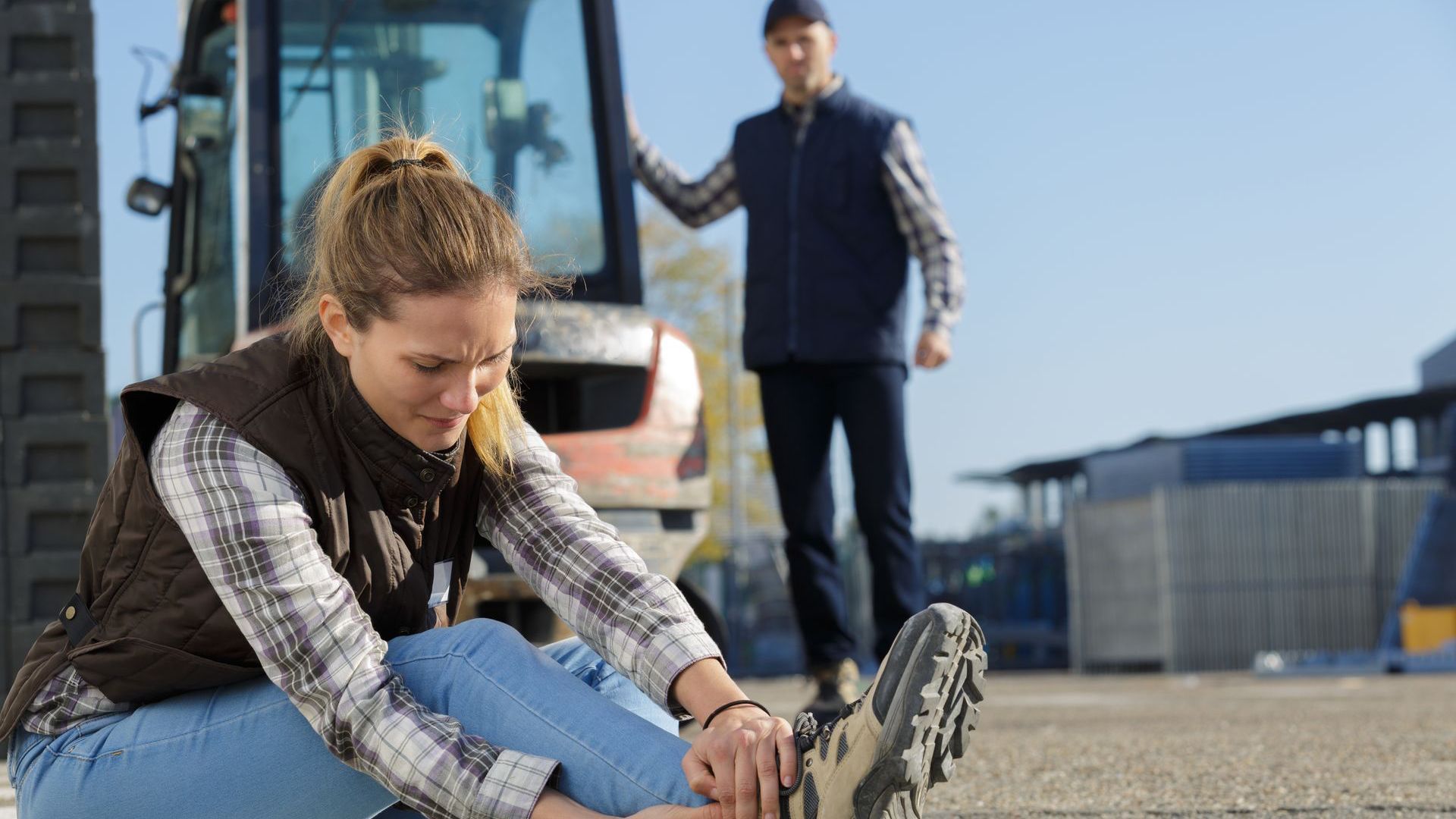 Woman seated on ground holding ankle, man near vehicle looking on.