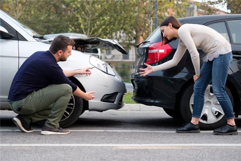 Two cars damaged in a collision; a man and woman assess the damage outdoors.