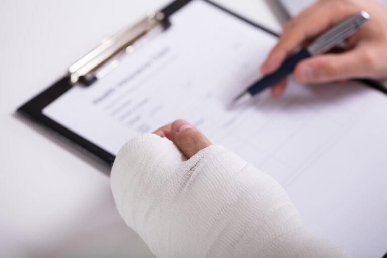 Person with bandaged hand writing on a clipboard.