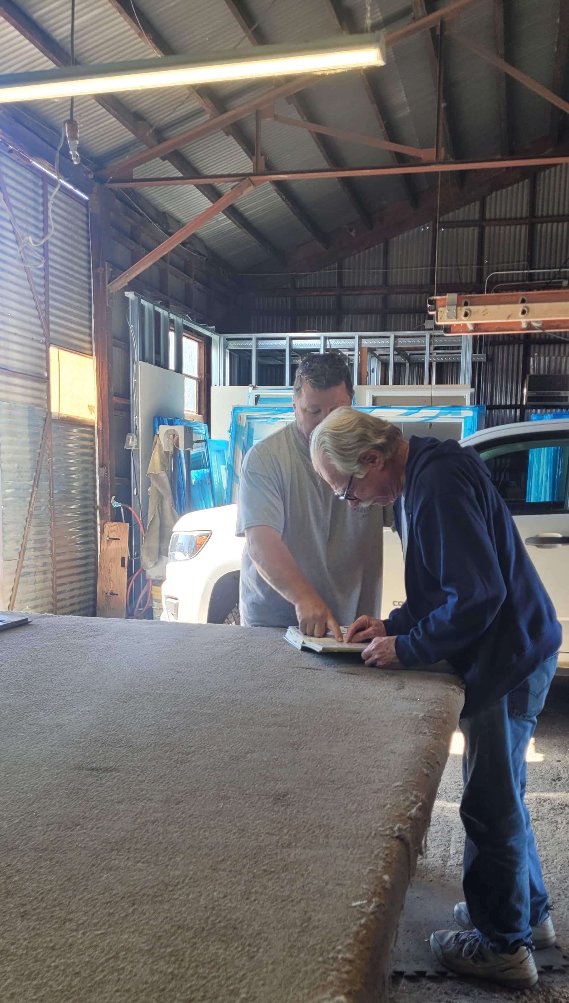 Two men are working on a piece of carpet in a garage.
