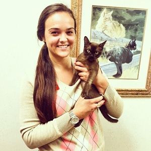 a woman is holding a cat in front of a painting of cats .