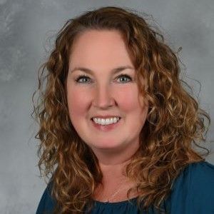 a woman with curly hair and a blue shirt is smiling for the camera .
