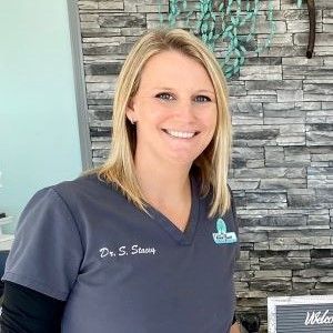 a woman in a scrub top is smiling in front of a stone wall .