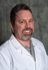 a man with a beard is wearing a white lab coat and smiling .