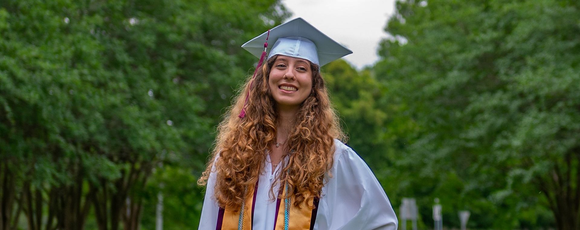 a woman in a graduation cap and gown is standing in front of trees .