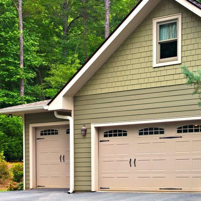 Tan house with a two-car garage and single side door, set against a wooded background.