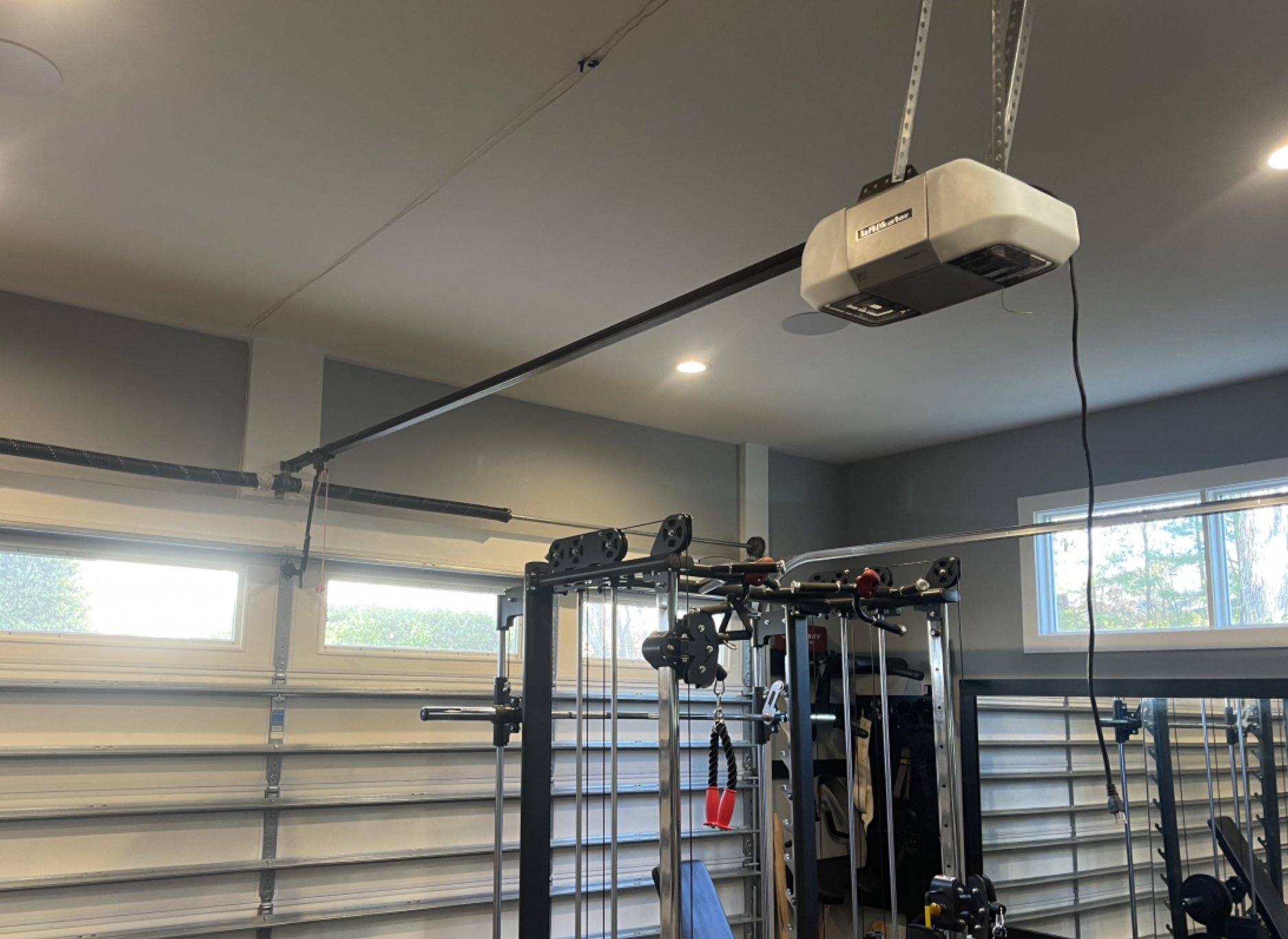 Garage gym with mounted projector, weight rack, and exercise equipment near windows