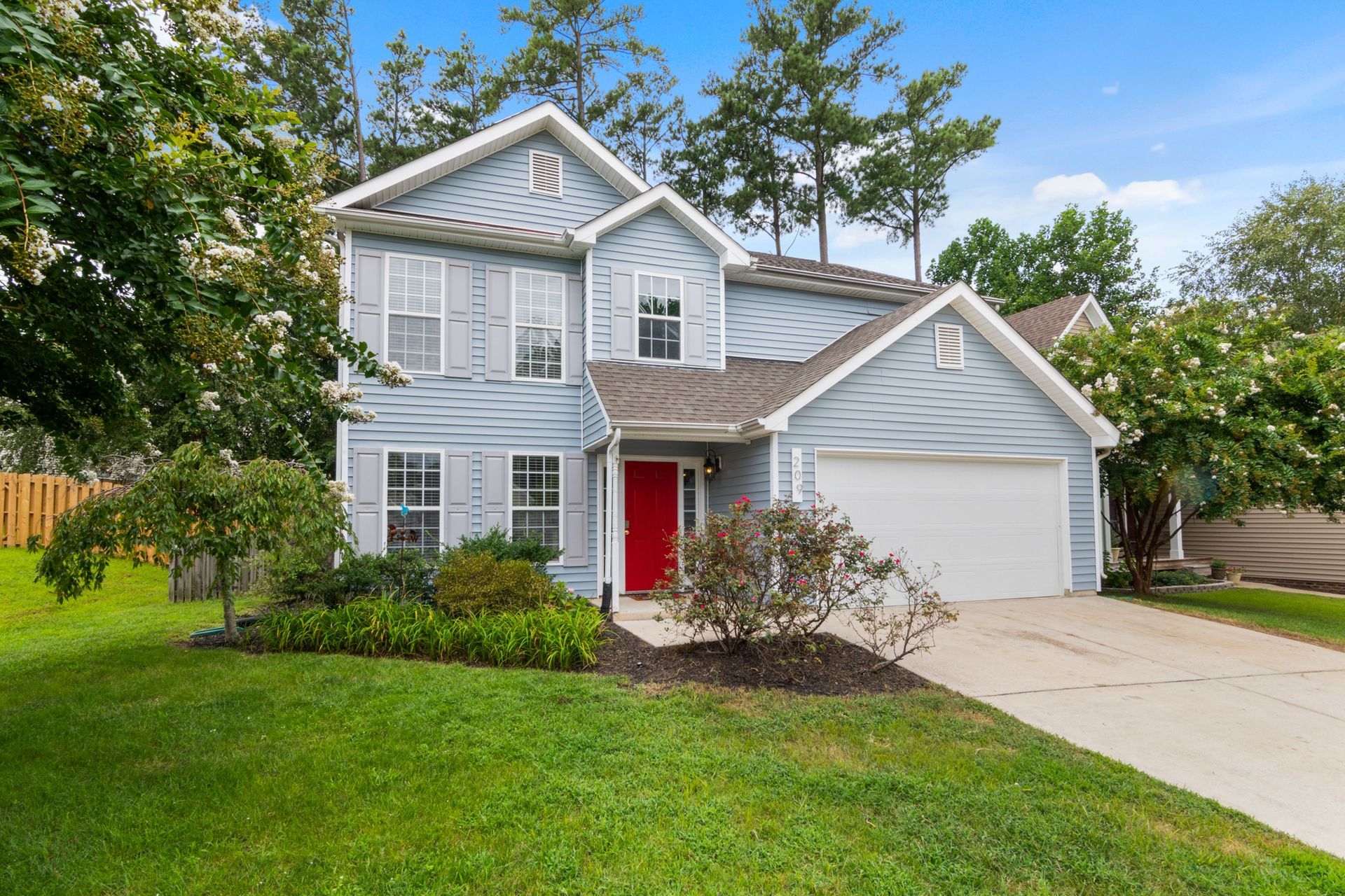 Two-story gray house with white trim, red front door, and attached garage in a green suburban yard
