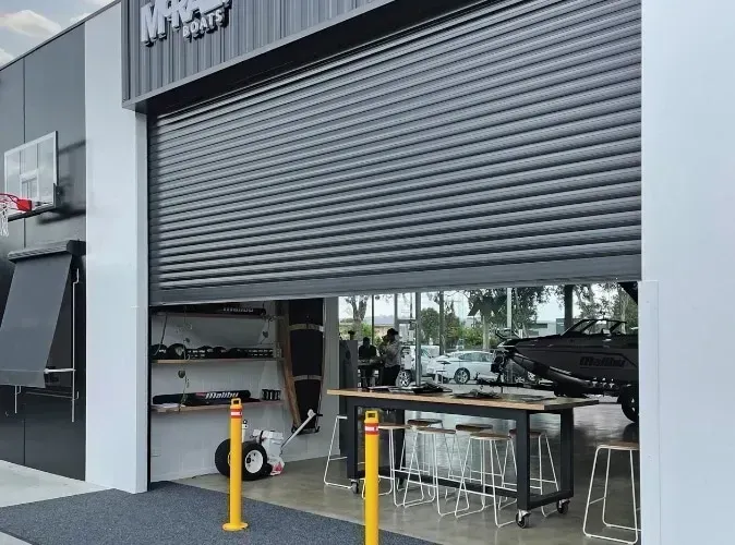 Gray roller shutter partially open, revealing a shop interior, people, and cars.