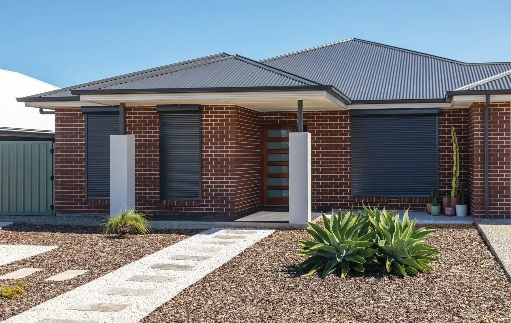 Modern brick house with dark roof, entry path, and landscaping on a sunny day.