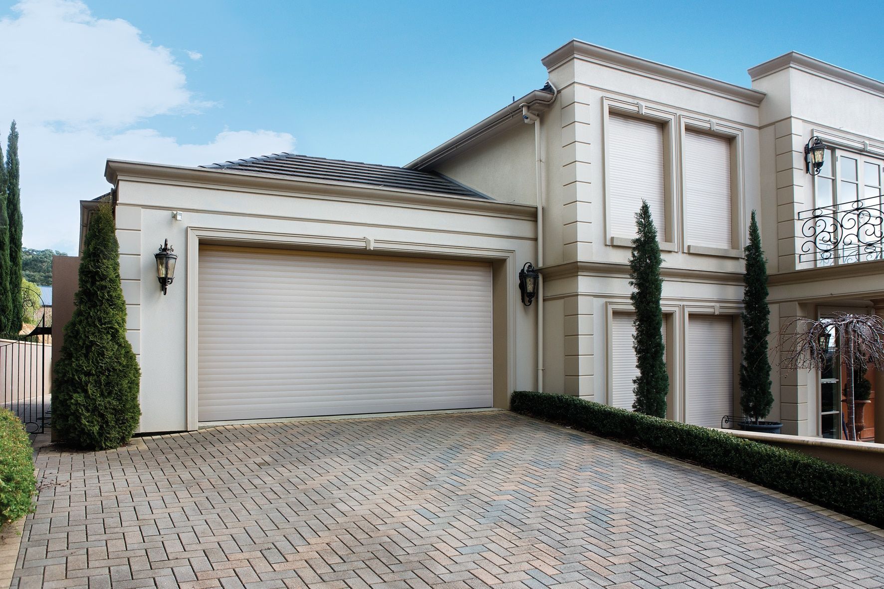 Beige luxury home with a brick driveway and a closed garage.