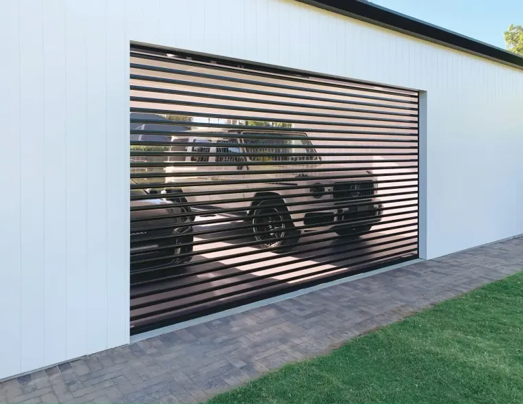 Garage with a roll-up, slatted door; a car is visible inside. White building exterior; brick and grass in front.