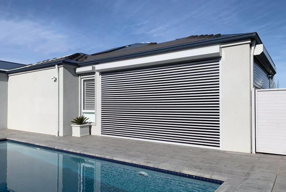 Exterior of a house with a closed, horizontal slat garage door next to a pool on a sunny day.