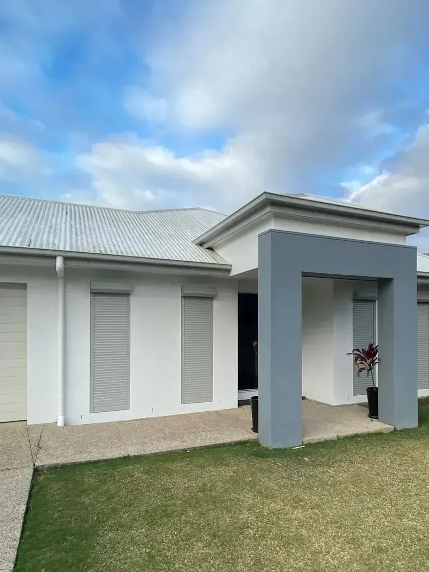 Modern white house with gray accents, garage, and front porch. Blue sky, green grass.