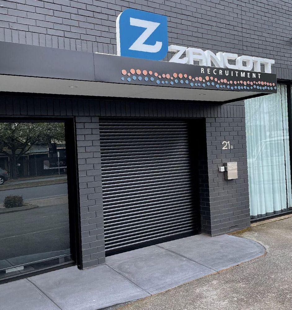 Exterior of Zancott Recruitment office, black facade, closed roller door, blue and white logo, address 21.