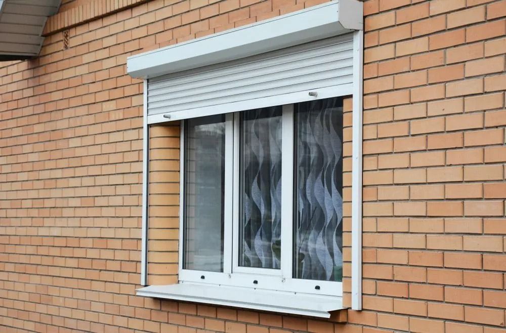 Window with closed white security shutters on a brick building.