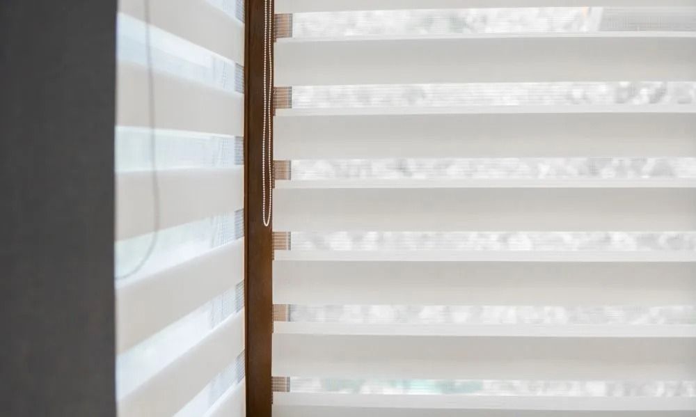 White and cream zebra blinds in a window frame, partially open.