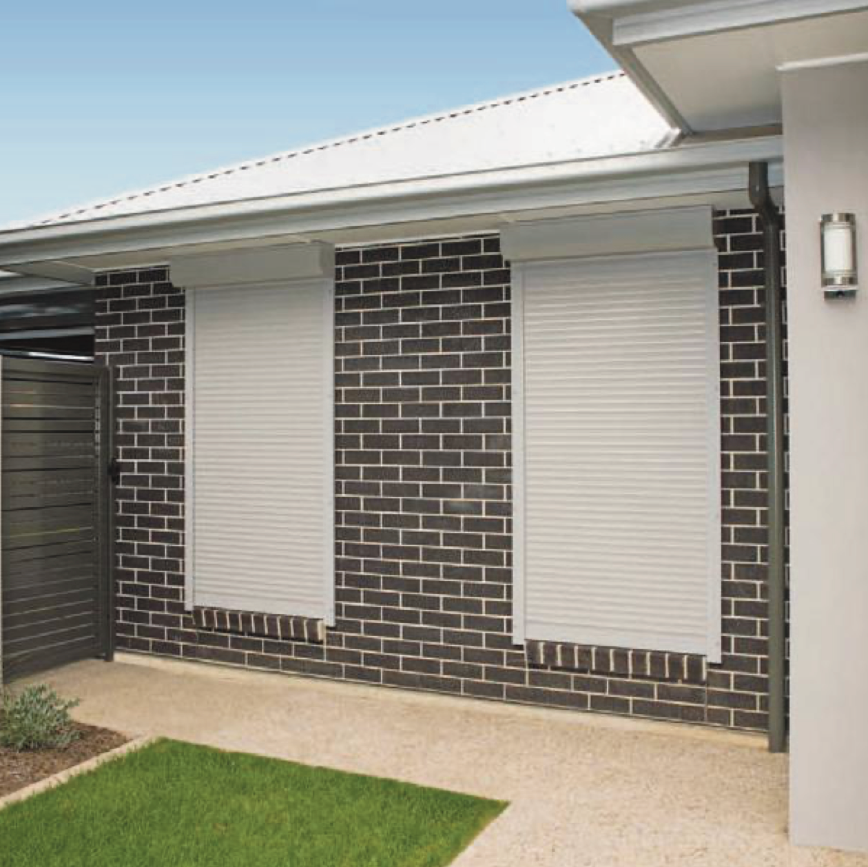 Exterior view of a brick house with two closed white roller shutters.