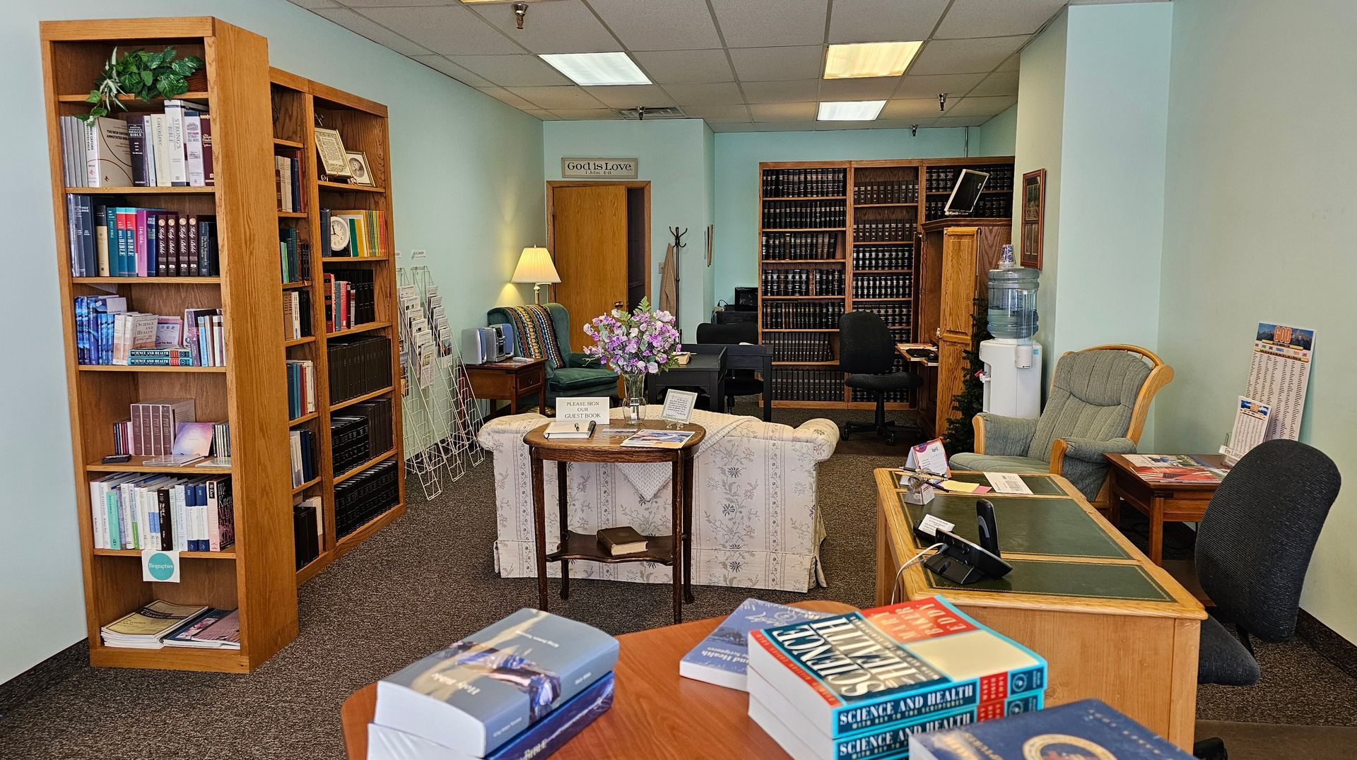 Cozy library lounge with bookshelves, chairs, a table, and a lamp in a carpeted room