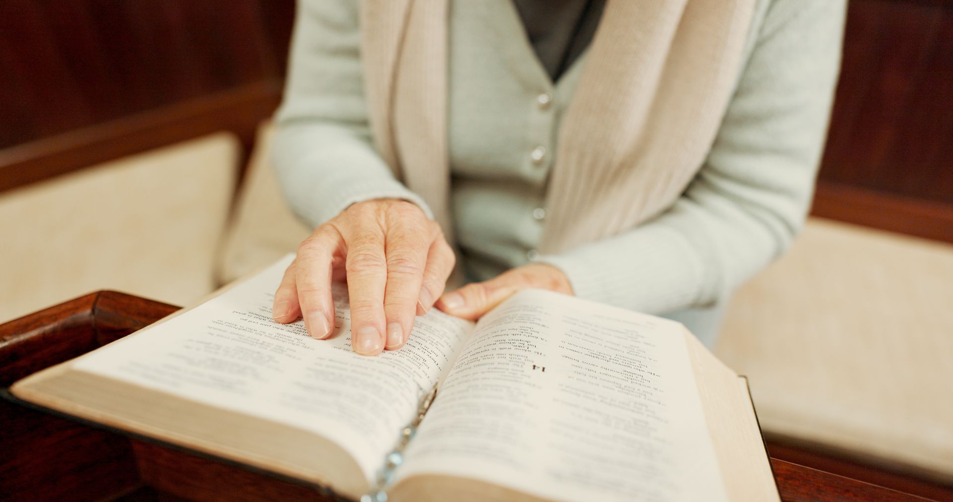 Person reading an open book at a wooden table, with a hand resting on the page.