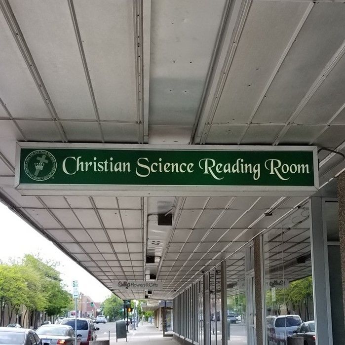 Green sign for Christian Science Reading Room under a covered sidewalk arcade.