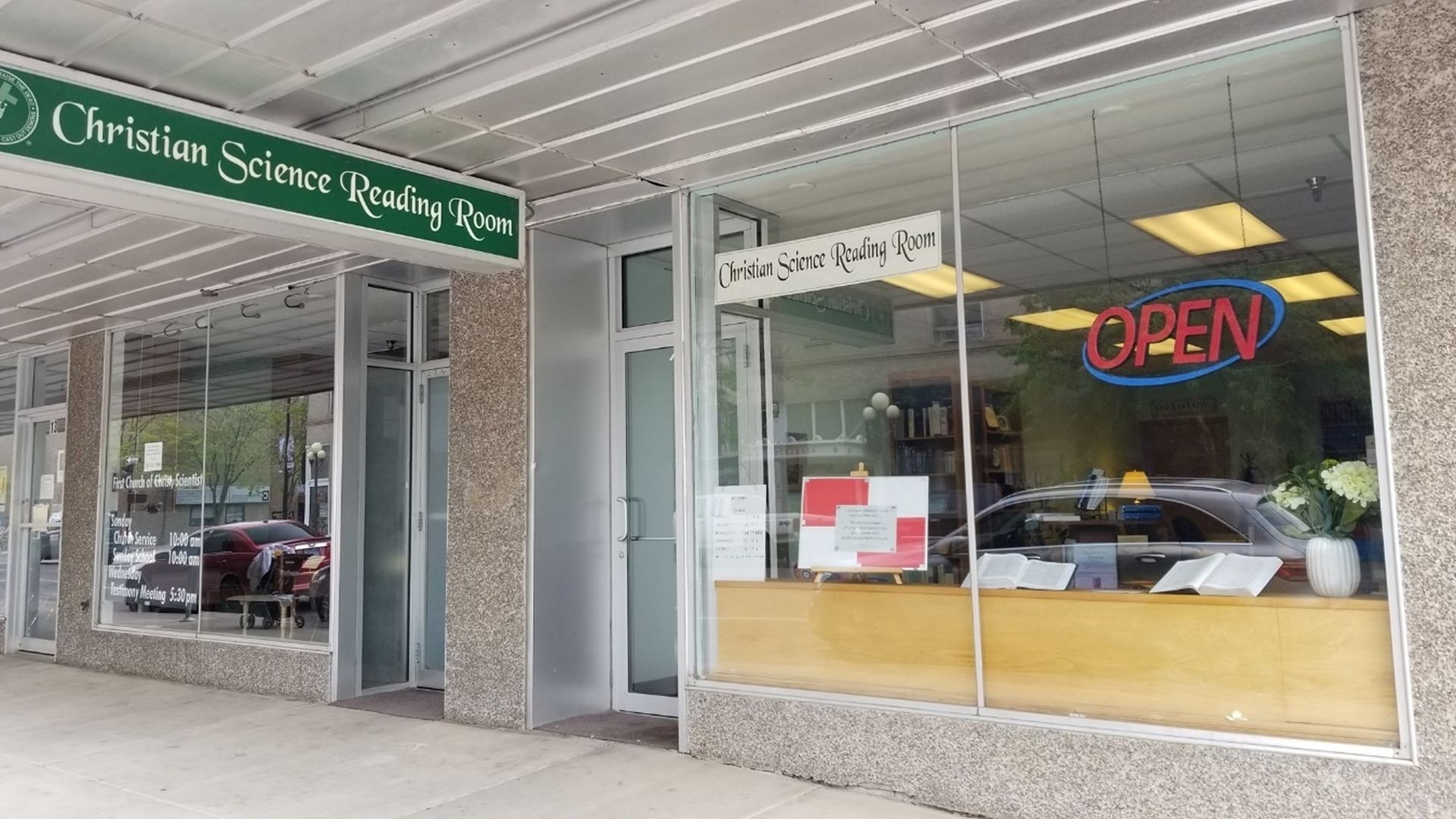 Storefront with green awning and neon “OPEN” sign in a strip mall.