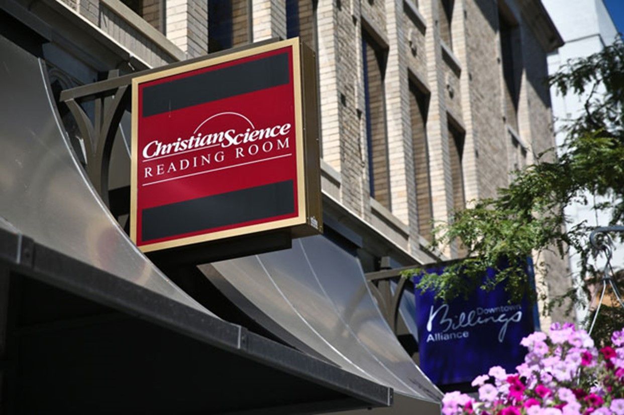 Christian Science Reading Room storefront sign on a brick building, with flowers in the foreground