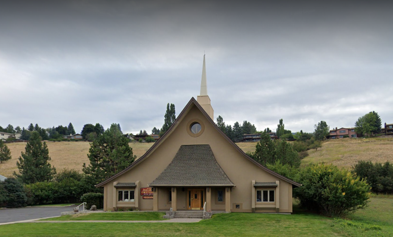 Small tan church with a steeple, centered in a grassy field under a cloudy sky.