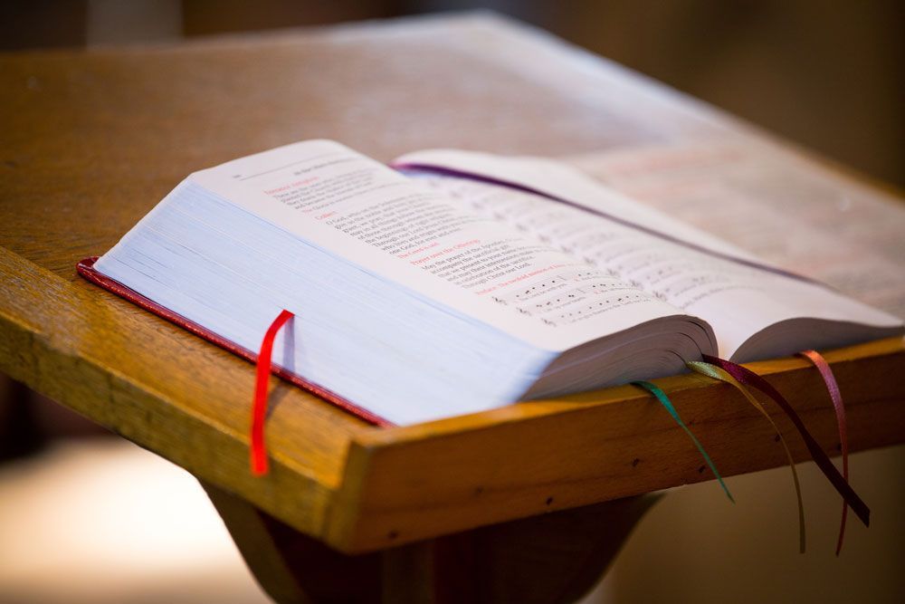 Open book with red ribbon bookmarks resting on a wooden table in soft light