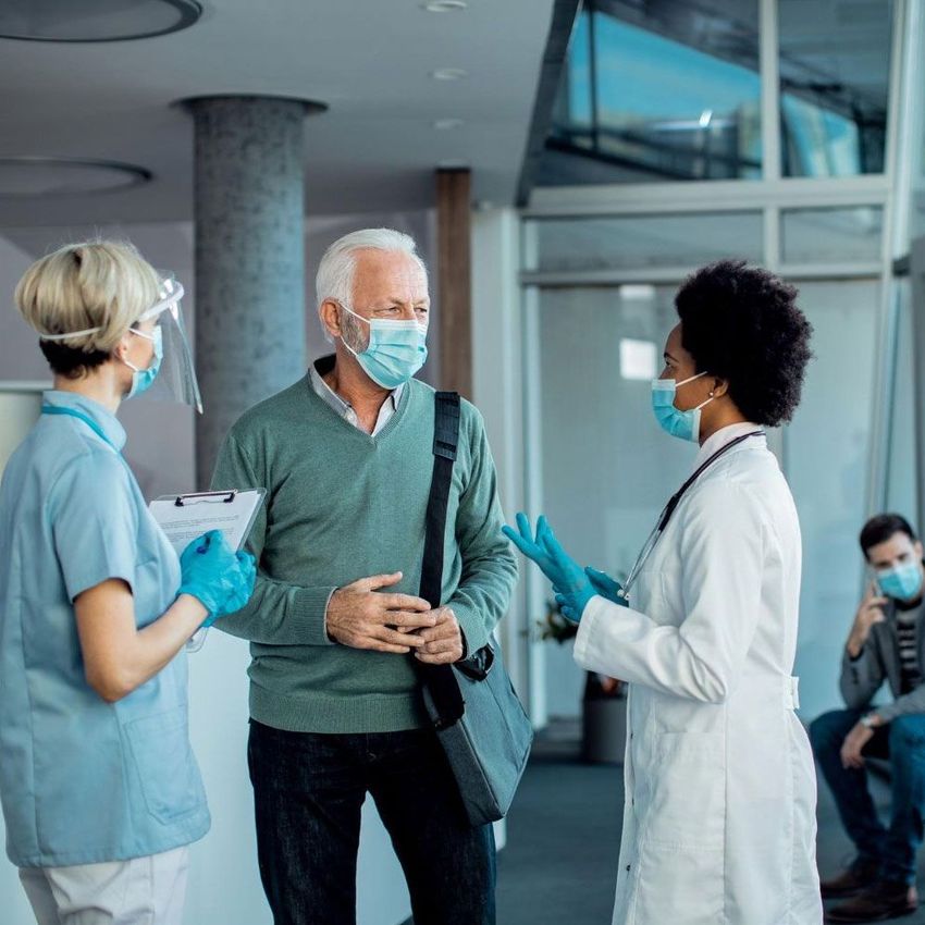 A group of people wearing face masks are talking to each other in a hospital lobby.