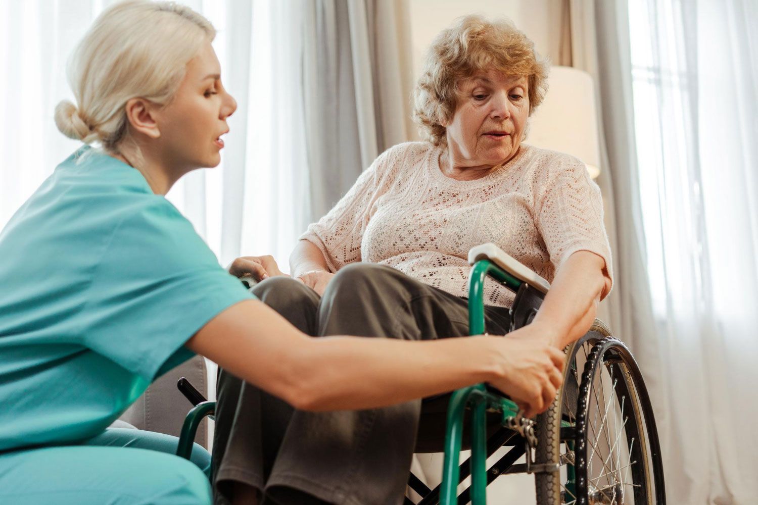 A nurse is helping an elderly woman in a wheelchair.