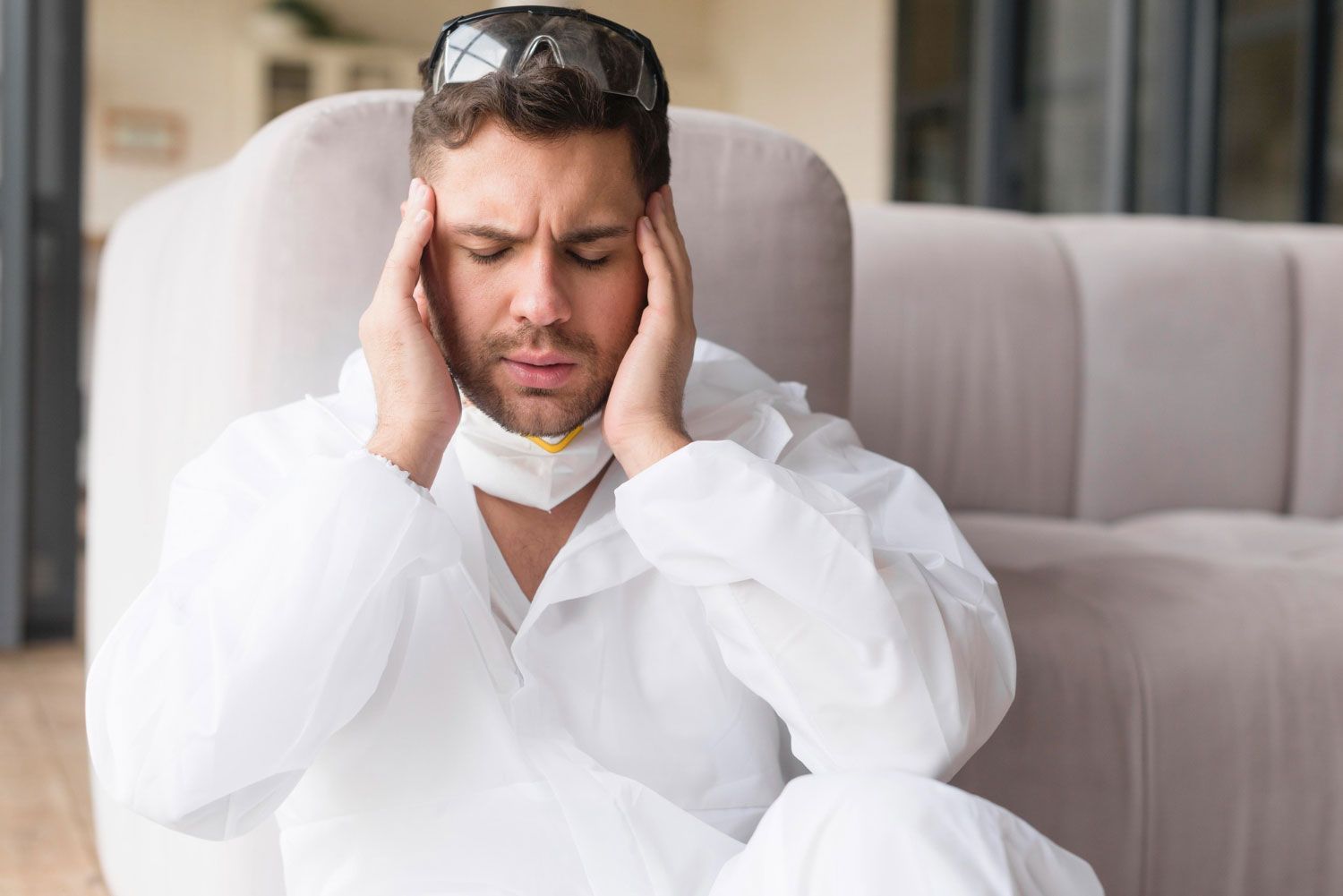 A man in a protective suit is sitting on a couch holding his head.