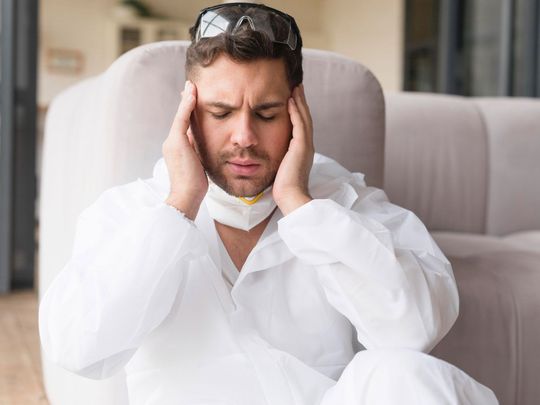 A man in a protective suit is sitting on a couch holding his head.