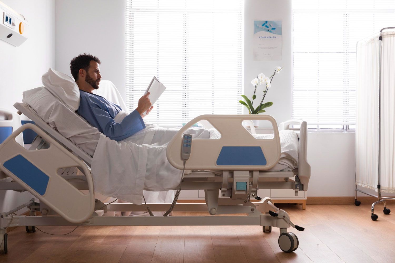 A man is laying in a hospital bed reading a book.