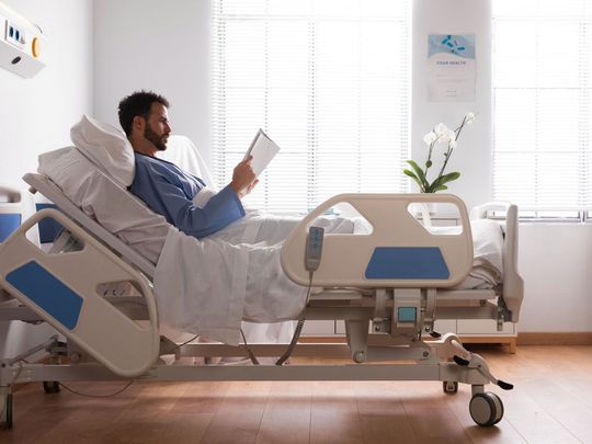 A man is laying in a hospital bed reading a book.