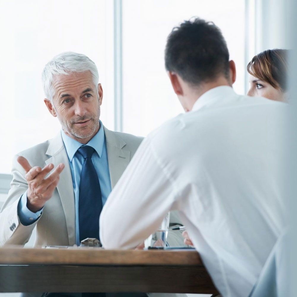 A man in a suit and tie is talking to two other men at a table.